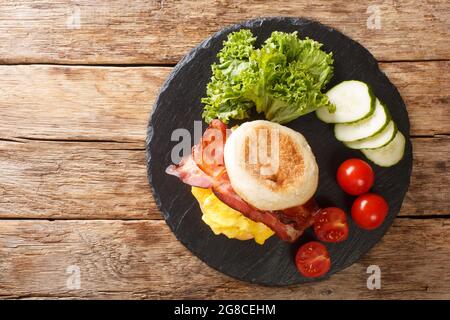 Primo piano di un sandwich per la colazione con uova strapazzate, pancetta e formaggio su un muffin inglese su una tavola di ardesia sul tavolo. Vista dall'alto orizzontale da abò Foto Stock