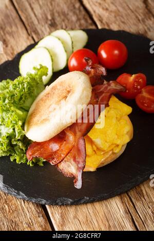 Sandwich inglesi appena sfornati con uova strapazzate, pancetta, formaggio e verdure primo piano su una tavola di ardesia sul tavolo. Verticale Foto Stock