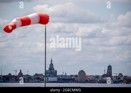 19 luglio 2021, Meclemburgo-Pomerania occidentale, Altefähr: Un ventoso si erge quasi orizzontalmente nell'aria e indica quindi un vento abbastanza forte. Sullo sfondo la silhouette della città anseatica di Stralsund. Foto: Stefan Sauer/dpa/ZB Foto Stock