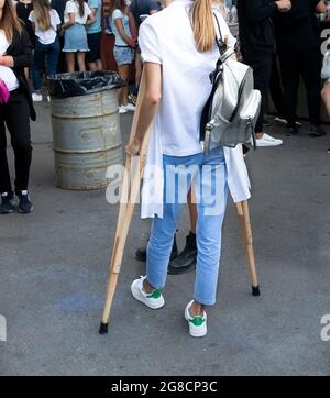 Una ragazza con una gamba rotta in un cast su stampelle è venuto al mercato. Viaggi di persone con disabilità. Adattamento dei disabili nella società moderna Foto Stock