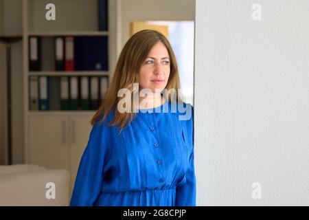Donna d'affari preoccupata in piedi in ufficio guardando fuori con un'espressione seria preoccupata mentre si appoggia contro il muro Foto Stock