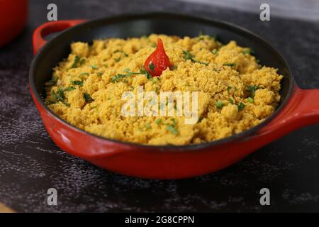 Pentola di ferro rossa con Farofa. Cucina tradizionale brasiliana. Su sfondo scuro. Foto Stock