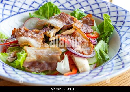 Lattuga verde fresca, verdure e insalata di pancetta fritta nella ciotola per pranzo su sfondo di tavola di legno. Foto Stock