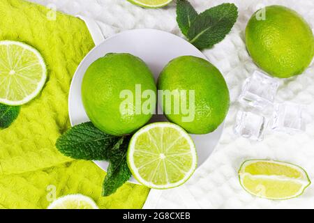 Vista dall'alto di lime fresche e succose verdi e fette di lime con foglie di menta in cucina su sfondo chiaro. Foto Stock