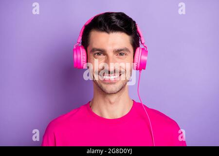 Foto di giovane allegro buon umore sorridente uomo che ascolta la musica in cuffie isolate su sfondo di colore viola Foto Stock