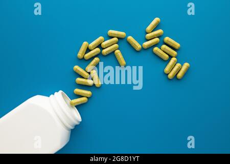 capsule di supplemento dietetico gialle versate dal vaso bianco senza marchio su sfondo blu. concetto di benessere mentale e di salute personale Foto Stock