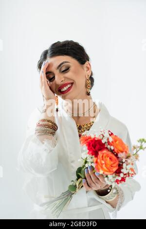 allegra sposa indiana con mehndi che tiene bouquet di fiori su bianco Foto Stock
