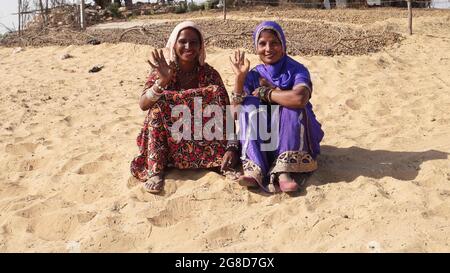 Due giovani femmine indiane con fazzoletti in campagna agitando le mani seduti sulla sabbia Foto Stock