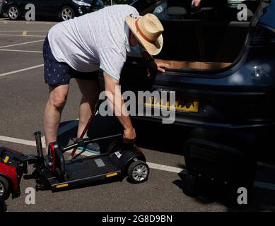 Bognor Regis, Regno Unito. 19 luglio 2021. Un genitore anziano si vede stendendo uno scooter per disabili usato da suo figlio (seduto in auto e non visibile) per riporlo nel bagagliaio. Credit: Joe Kuis / Alamy Reportage Foto Stock