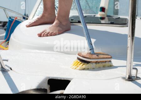 Uomo lavando barca bianca con spazzola e sistema di acqua a pressione al molo. Concetto di manutenzione yacht. Foto Stock