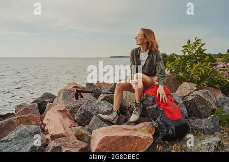 Il viaggiatore è rimasto soddisfatto riposandosi sulle rocce con il suo zaino Foto Stock