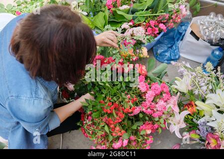 Fiorista femminile che lavora con fiori all'aperto, decorando eventi con fiori Foto Stock