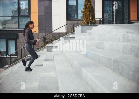 Sportiva con grappoli afro alla moda che salgono i gradini di cemento Foto Stock