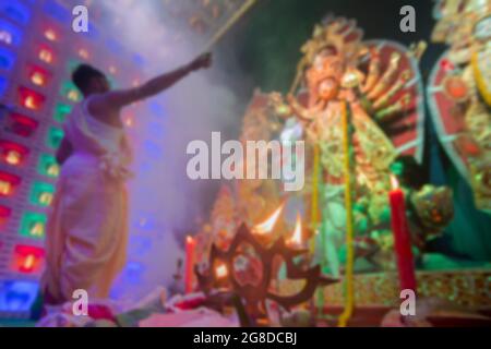 Immagine offuscata di Panchpradip, illuminata, mentre fuori di foucs giovane indù Bengalese purhit adorazione Dea Durga, Durga aarti dentro puja pandal, girato a D. Foto Stock