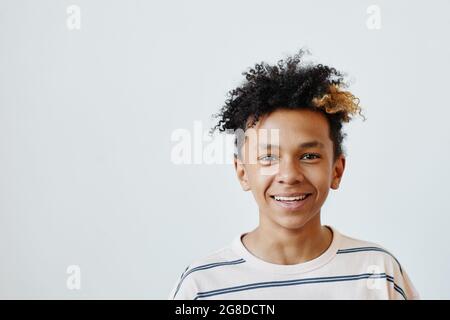 Ritratto minimo di ragazzo di razza mista che sorride alla fotocamera su sfondo bianco, copia spazio Foto Stock