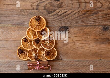 Albero di Natale alternativo. Vista dall'alto dell'albero di Natale fatto da stella di anice, bastoncini di cannella, arancio secco su sfondo di legno. Spazio per la copia, disposizione piatta. Foto Stock