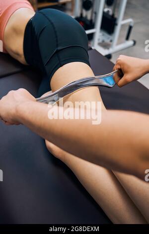 Massaggio medico alla gamba della donna con utensile in acciaio nel centro di fisioterapia. Fisioterapista maschile Foto Stock