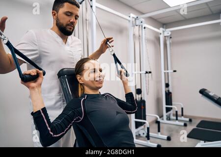 Il kinesiologist assiste la giovane donna a fare esercizi per trattare i muscoli delle mani e la spina dorsale. Paziente femminile Foto Stock