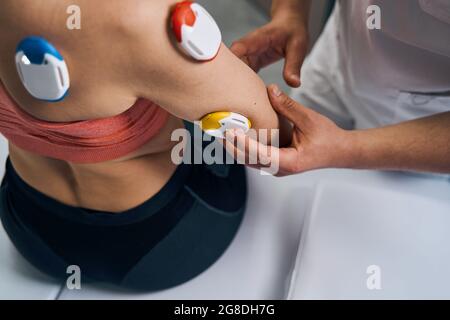 Fisioterapista installa un elettrostimolatore sul braccio della giovane donna. Massaggio con elettrostimolatore Foto Stock