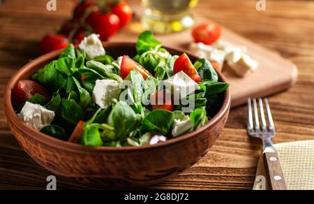 Insalata di foglie di lattuga fagiolo, formaggio, pomodori ciliegini, in una ciotola di ceramica su una tavola di legno da vicino (Valerianella locusta). Dieta e ea sana Foto Stock