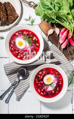 Zuppa estiva di barbabietole fredde con panna acida e uova su fondo di piastrelle bianche. Cucina russa. Vista dall'alto. Foto Stock