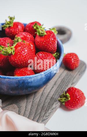 Fragole mature in ciotola blu su tavola rustica in legno, stile elegante, frutti di bosco dolci per dessert estivi. Ciotola o piatto riempito con fragole rosse fresche. Foto Stock