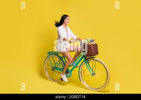 Foto laterale profilo full size di affascinante bella ragazza Rise bicicletta copyspace isolato su sfondo di colore giallo Foto Stock