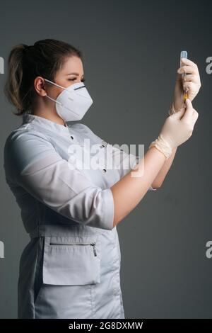 Studio Veretical shot di infermiere in guanti bianchi e maschera facciale che tiene e riempie il vaccino a siringa su sfondo nero isolato. Foto Stock
