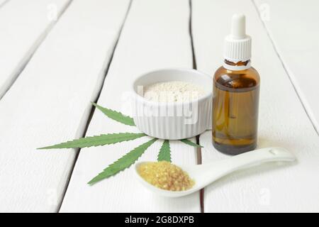 Cucina con concetto di cannabis. Prodotti infusi di erbe infuse - olio di thc, farina di marijuana, zucchero su sfondo bianco con spazio di copia Foto Stock