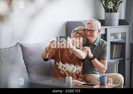 Ritratto di coppia senior moderna prendendo selfie a casa in interni minimal, spazio di copia Foto Stock