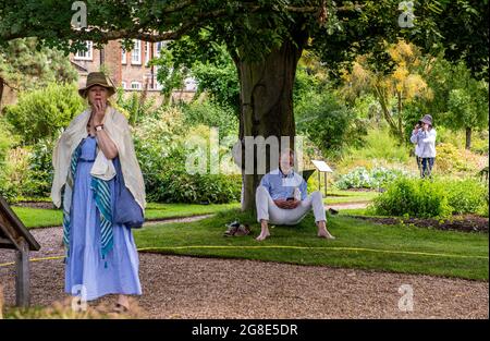 Una donna che guarda perplessa, un uomo che legge da un albero e un'altra donna che parla sul suo telefono sullo sfondo nel Chelsea Physicic Garden a Londra. Foto Stock