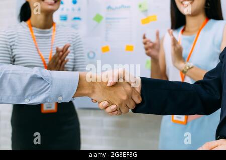 Giovani asiatici uomo d affari e business donna dando un gesto di handshake e rasserenanti lavoratori aziendali battendo le mani sullo sfondo della sala meeting Foto Stock