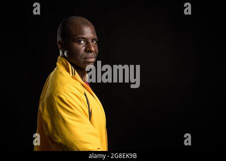 Vista laterale di un uomo afro-americano in piedi guardando la fotocamera sfondo nero Foto Stock