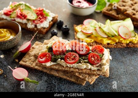 Angolo di vari gustosi toast di pane croccante con verdure fresche mature poste sul tavolo per uno spuntino vegetariano Foto Stock