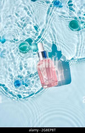 Mockup di bottiglia cosmetica rosa in vetro con pipetta e siero su superficie d'acqua con onde concetto di pubblicità detergente e idratante, invecchiamento nativo s. Foto Stock