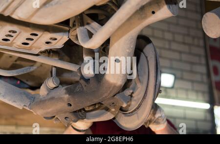 Aste posteriori trasversali e longitudinali inferiori arrugginite su una vecchia vettura. Nel garage, un uomo cambia le parti di un veicolo. Concetto di piccola impresa, servizio di riparazione auto e manutenzione. 4K UHD. Foto Stock