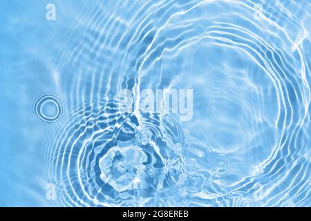 Tessuto della superficie dell'acqua trasparente di colore blu chiaro sfocato. Onde d'acqua alla luce del sole. Foto Stock