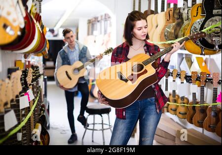 i clienti adolescenti decidono di utilizzare una chitarra acustica adatta nel negozio di chitarra Foto Stock