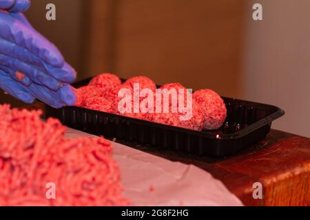 Primo piano di una mano di donna con un guanto blu che fa polpette con carne macinata Foto Stock