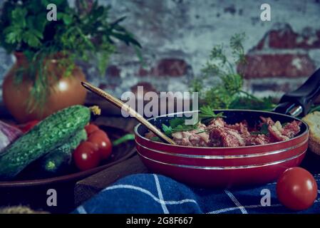 Una padella con carne stufata e verdure ed erbe varie sullo sfondo di un muro di mattoni. Foto Stock