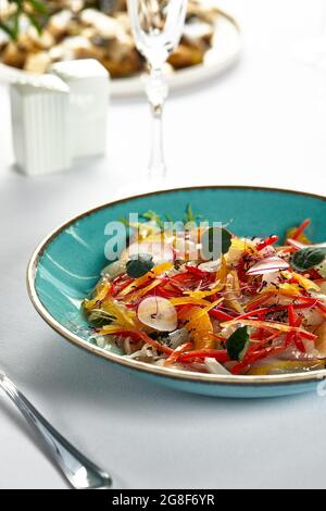 Ceviche di spigola con verdure tritate finemente, primo piano di marinata di filetto di spigola fresca su un piatto blu. Foto Stock