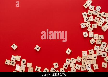 Immagine di sfondo le lettere sono sparse in disordine. Lettere inglesi. Lettere quadrate di legno su sfondo rosso brillante. Biglietto d'auguri, pronto all'uso Foto Stock