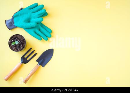 composizione di attrezzi da giardinaggio e guanti verdi su sfondo giallo Foto Stock