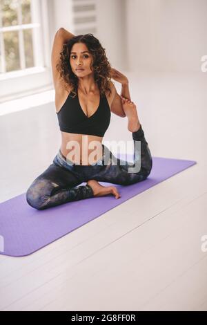 Giovane donna che fa yoga asana in classe di fitness. Fit femmina che pratica yoga, facendo una zampe re piccione posa al centro benessere. Foto Stock