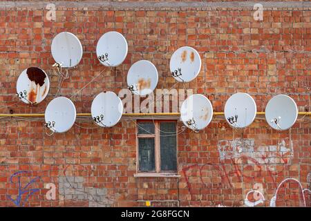 Molti piatti satellite sono attaccati al muro di una vecchia casa. Foto Stock