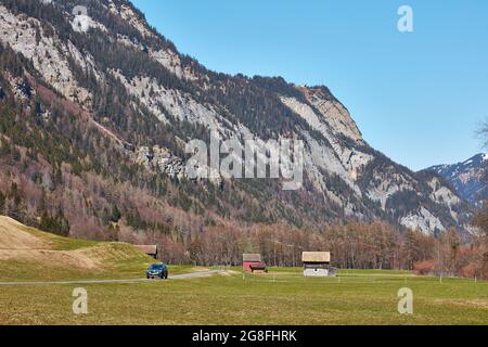 Auto che passa fienili rurali in alta valle Taminatal vicino Vaettis con la stazione superiore della funivia Feuscha su Vaettnerber Foto Stock