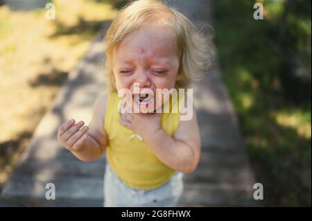 Primo piano ritratto di piccolo divertente bambina bionda bambina in tuta gialla piangendo all'esterno in estate. Tantrum infantile. Concetto sano di infanzia Foto Stock