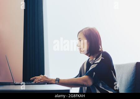 Donna anziana che lavora su un computer portatile a casa. Foto Stock