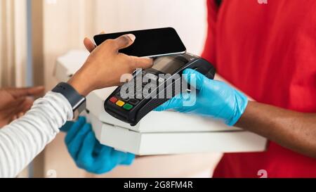 Lady Paying Courier con smartphone e Terminal Receiving Pizza Indoor Foto Stock