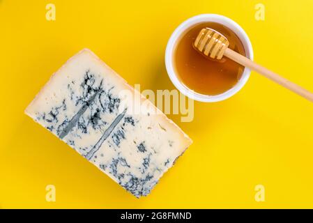 Gorgonzola italiana, fetta di formaggio a muffa blu con ciotola al miele con cucchiaino di miele su sfondo giallo, vista dall'alto, piatto, spazio copia Foto Stock